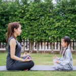 Family Asian Mother teacher training yoga child daughter on a yoga mat at home garden